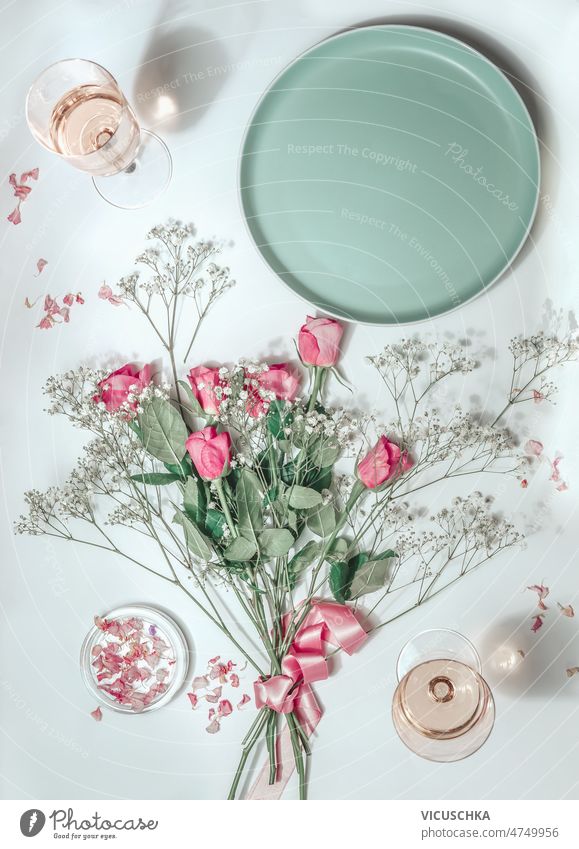 Flowers bunch with pink roses , empty plate and rose wine in glasses in sunlight aesthetic flat lay flowers bunch wineglasses white background top view petal