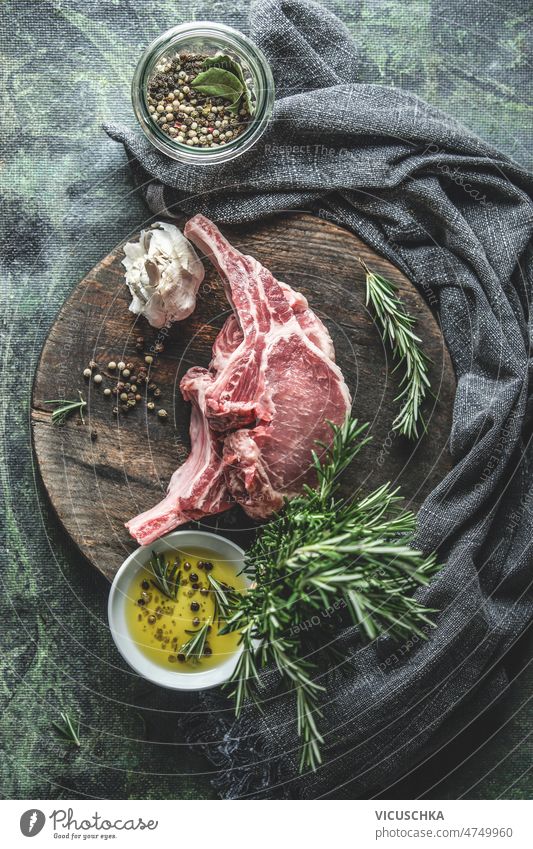 Iberico pork racks on round wooden cutting board with rosemary, olive oil, garlic and pepper raw meat iberico pork kitchen table dish cloth cooking preparation