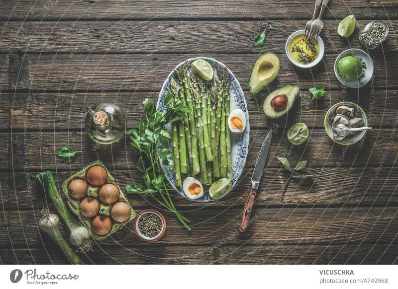 Green asparagus with halves boiled eggs, lime and herbs on plate with knife and other healthy ingredients green avocado spring onion olive oil spices bowls