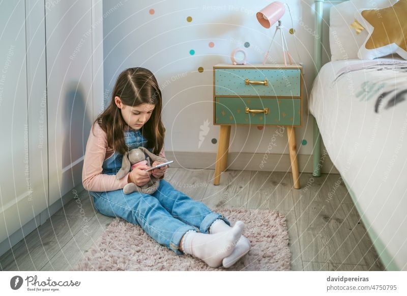 Little girl using mobile while hugging her stuffed animal sitting on the floor little play mobile phone toy bedroom child kid smartphone cellphone looking game