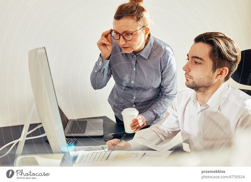 Two business people discussing financial data looking at computer screen. Businesswoman talking to young male coworker in office. People entrepreneurs having conversation working together
