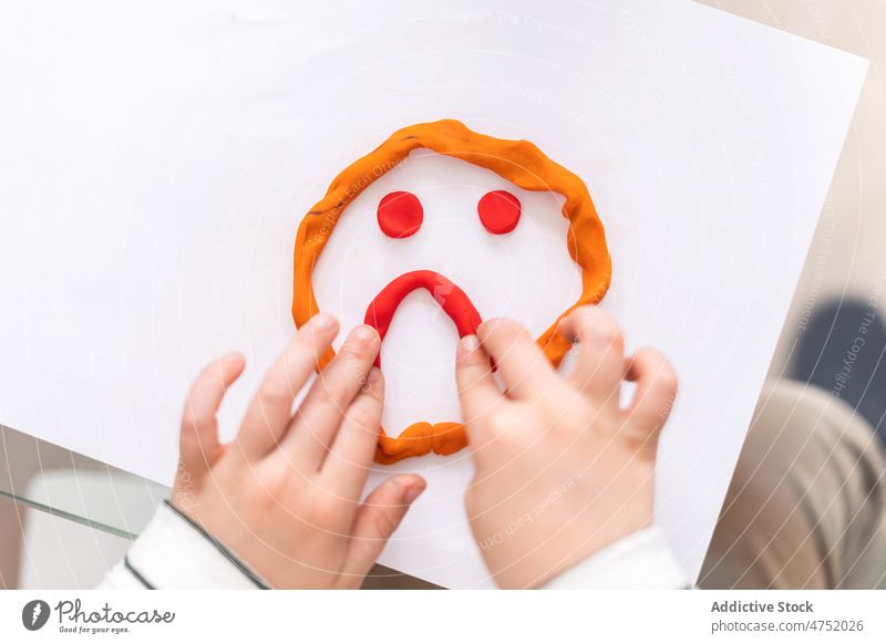 Anonymous child pointing at sad face plasticine diagnostic childhood visit choose mood room appointment mental light session paper patient table creative form