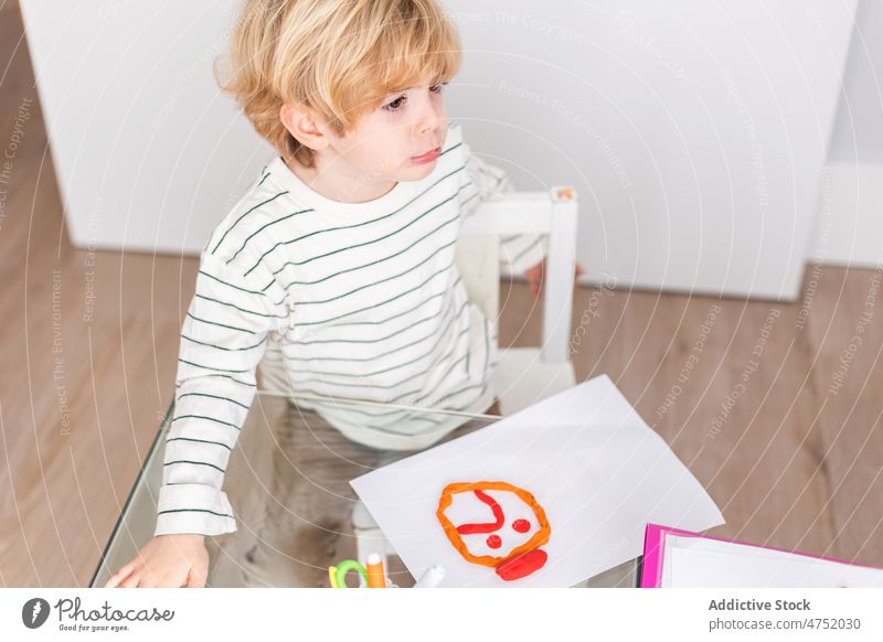Boy making sad face with red plasticine on white paper boy child diagnostic childhood visit choose mood room appointment mental light session patient table