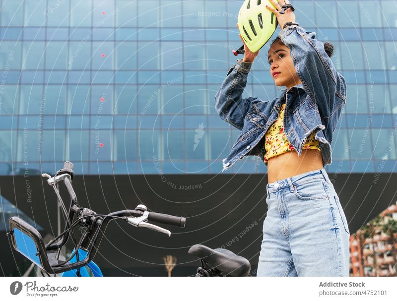 Ethnic woman taking on helmet for practicing bicycle ride put on activity modern style leisure hobby pastime female prepare transport safety protect active