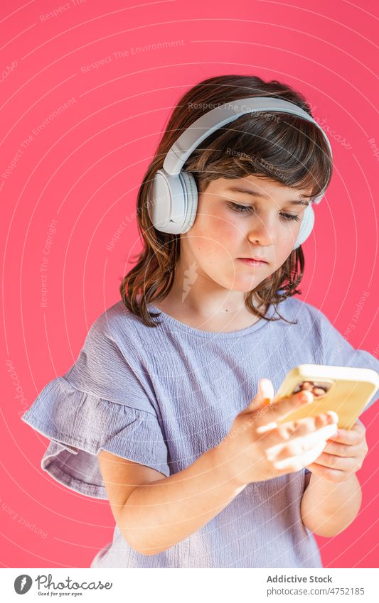 Little girl listening to music in headphones and reading message using wireless search smartphone bright song playlist digital browsing leisure watch studio
