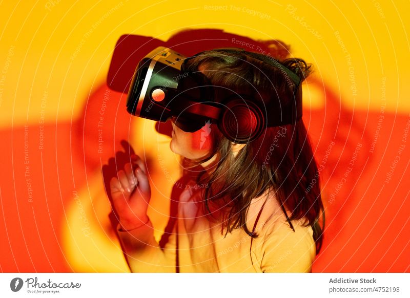 Little gamer in VR glasses boy vr lean wall watch videogame explore red light neon illuminate color child girl kid monochrome female bright headset entertain