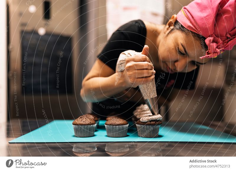Hispanic woman squeezing cream on muffins baker decorate cupcake pastry bag bakehouse table squeeze dessert female sweet chocolate cuisine culinary food
