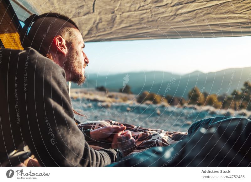 Bearded male hiker enjoying nature from tent at sunrise man camp hill admire trekking adventure relax traveler tourism contemplate valley landscape observe