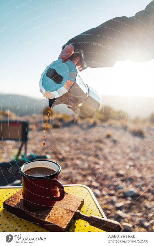 Person pouring aromatic coffee from moka pot in campsite hiker hot breakfast brew morning explore person cup mug coffee maker journey beverage tourism camper