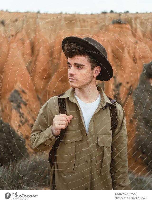 Young man spending time in countryside tourist explore travel weekend wanderlust rock adventure portrait male discover mountain trip backpack hat shirt hike