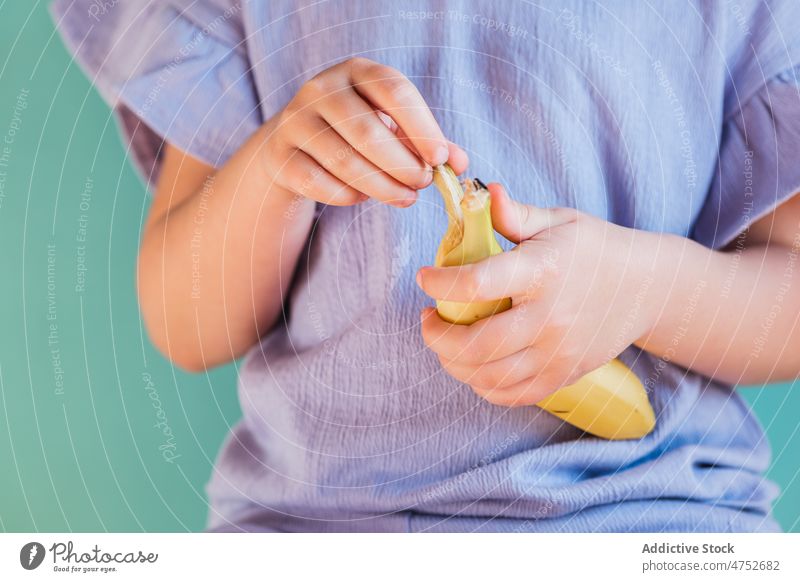 Anonymous girl peeling ripe banana kid fruit healthy food childhood natural organic nutrition style cute innocent light studio sweet bright color wall colorful