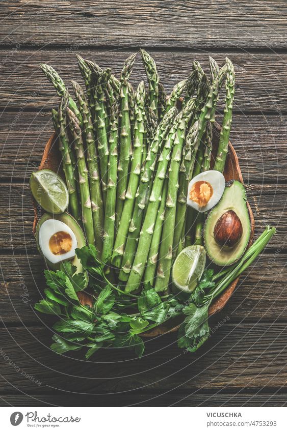 Green asparagus bunch with egg halves, avocado, parsley and lime on rustic woode kitchen table. Healthy cooking green healthy preparation seasonal spring