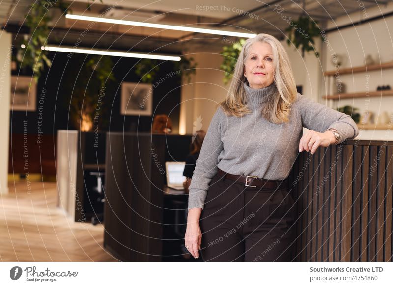Portrait of senior white businesswoman woman with focused expression leaning on office partition in modern coworking space business owner portrait look indoors