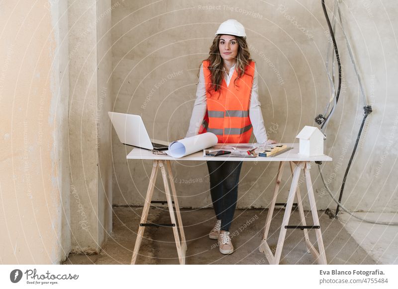 professional confident architect woman in construction site working on blueprints. Home renovation workspace protective helmet protective jacket mobile phone