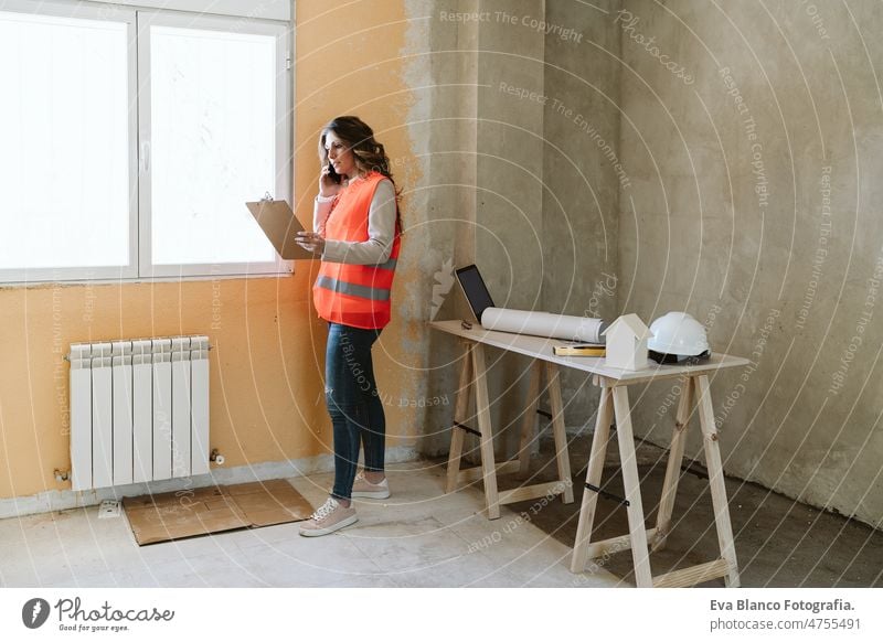 professional architect woman in construction site talking on mobile phone holding blueprints workspace protective helmet protective jacket real estate caucasian