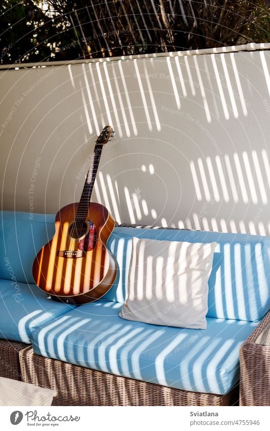 An acoustic guitar stands on a blue sofa next to a pillow on the terrace style space design interior background apartment wood copy textile white home old decor