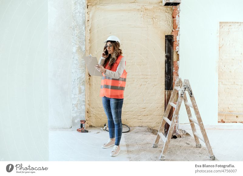 architect woman in construction site talking on mobile phone and blueprints.Home renovation technology confident workspace protective helmet protective jacket