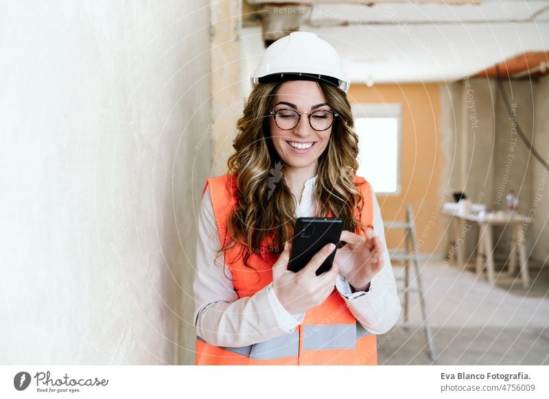 professional architect woman in construction site using mobile phone and blueprints.Home renovation technology confident workspace protective helmet