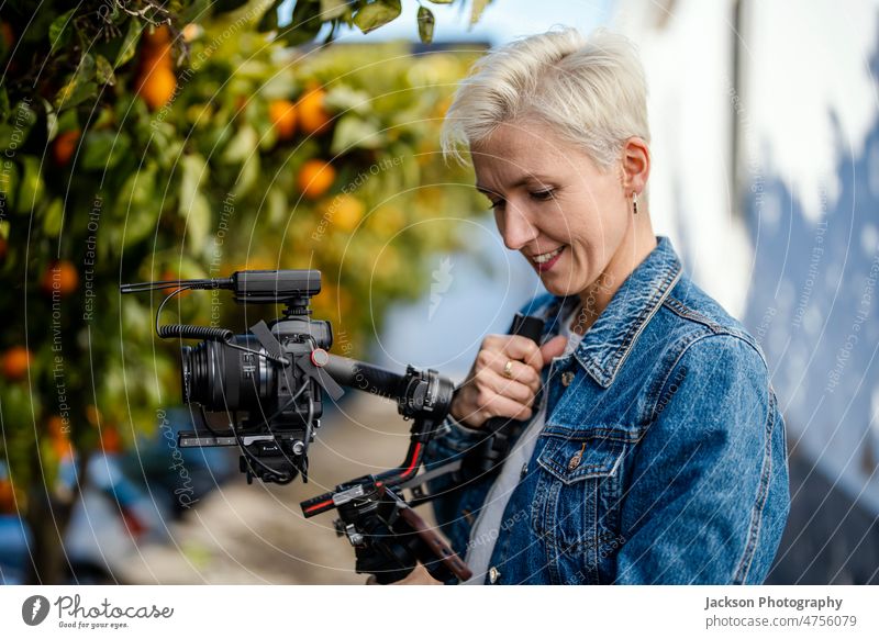 Camera operator with movie setup outdoor film maker video woman equipment microphone camera orange orange tree portrait hipster cap stabilized