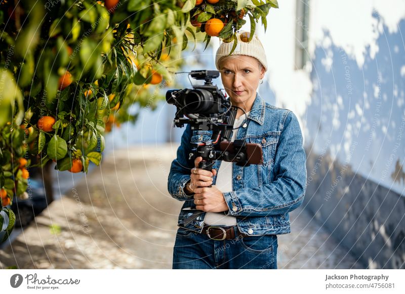 Camera operator with movie setup outdoor film maker video woman equipment microphone camera orange orange tree portrait hipster cap stabilized