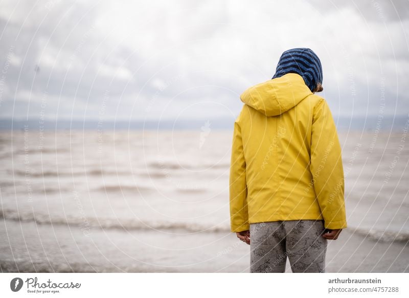 Child in rainwear on beach in cloudy weather Infancy Rain Sky Moody Waves Water Wind windy windy weather Surface of water Nature Clouds Exterior shot Ocean