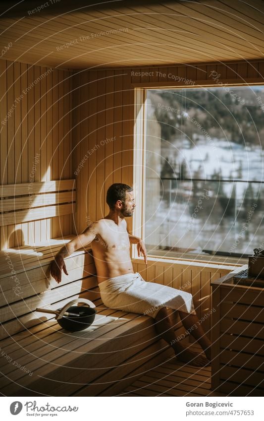 Young man relaxing in the sauna and watching winter forest through the window caucasian body relaxation bath finland therapy finnish healthy beauty wood water