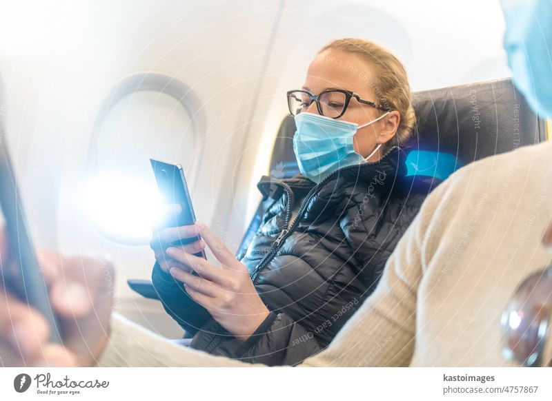 A young couple wearing face mask, using smart phone while traveling on airplane. New normal travel after covid-19 pandemic concept. traveler tourist transport