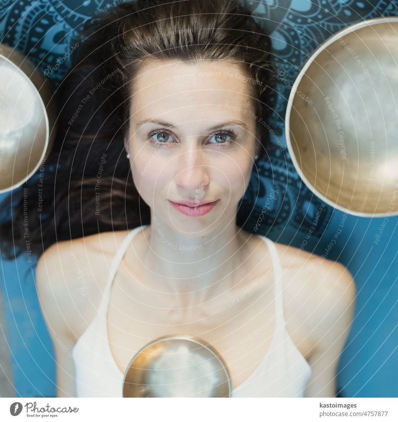 Yoga concept, meditation and sound therapy. Portrait of beautiful young caucasian woman surrounded by copper tibetan singing bowls and instruments buddhism