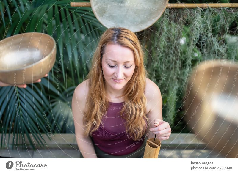 Yoga concept, meditation and sound therapy. Beautiful young caucasian woman surrounded by copper tibetan singing bowls and instruments buddhism meditating
