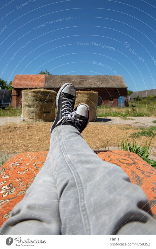 Legs with gray jeans and chucks on a farm Farm relax Summer Hay Straw Country life snotty Rural Landscape Nature Exterior shot Harvest Agriculture country bale