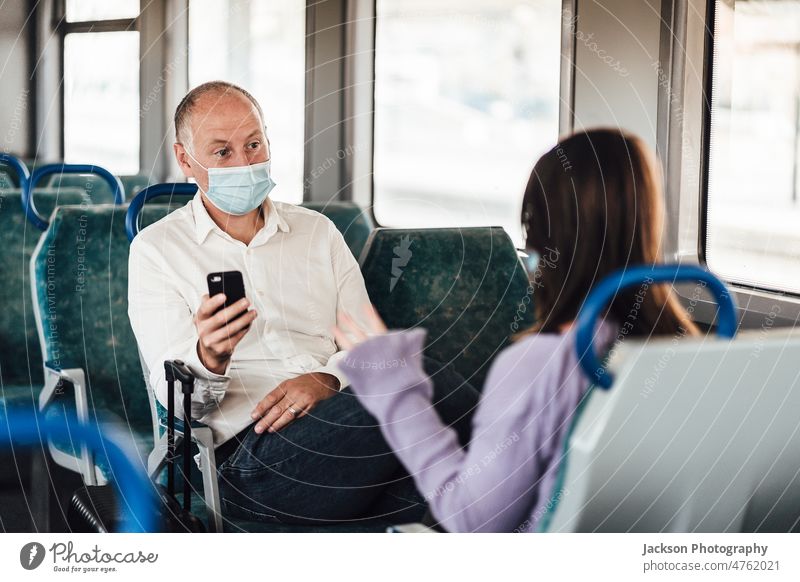 A couple of friends wearing mask and talking while traveling by train woman conversing chat women female bag luggage smartphone sitting new normal vacation