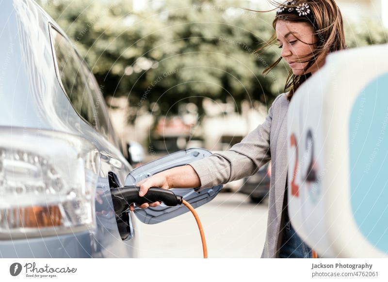 A woman charging an electric car in urban settings socket close-up recharging rechargeable young charger ecology clean electricity cable supply battery plug