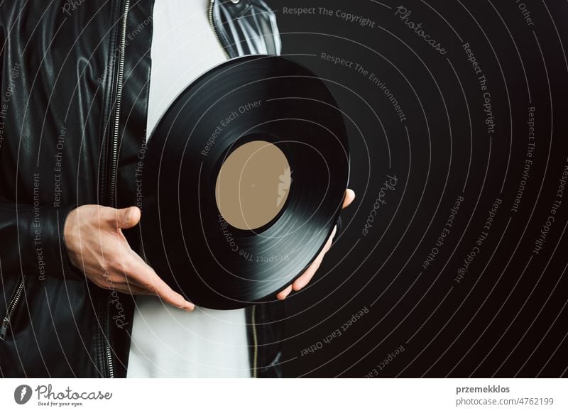 Man holding vinyl record. Vintage music style. Rock style. Male wearing black jacket holding black disc standing on dark background. Retro music disk sound