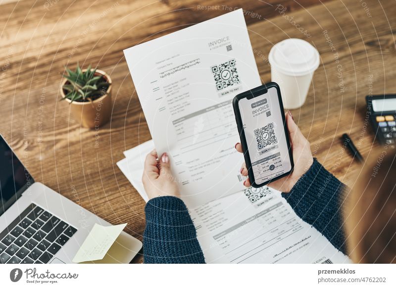 Woman paying invoice scanning QR code from document using fast secure payment system and smartphone QR scanner. Business woman paying bills using express payment technology. Paying expenses online