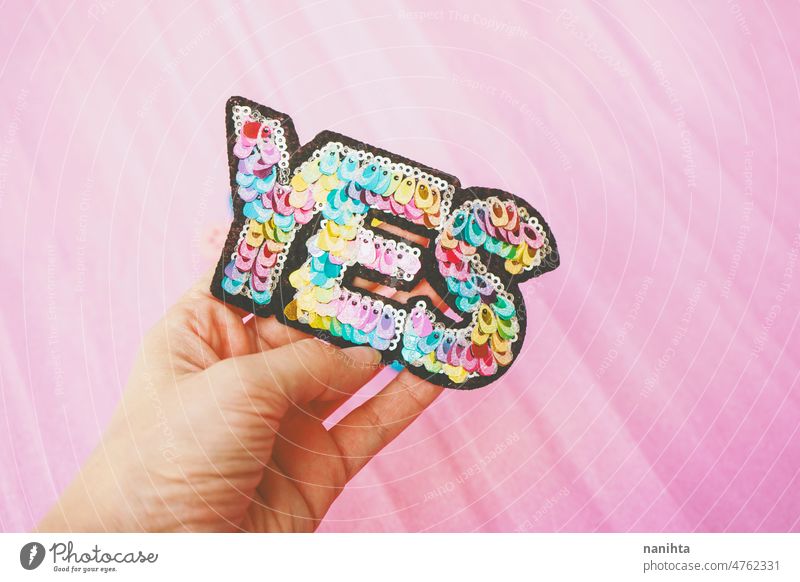 Word "yes" make with colorful sequins against pink background word diy fashion trendy patch positive attitude optimism optimist positivity pastel tones hands