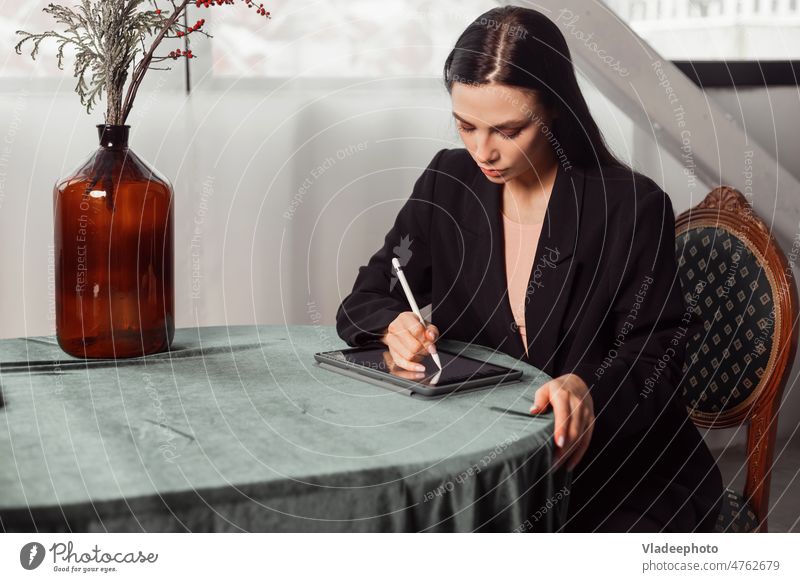 Young brunette freelancer woman designer draws sketches on a graphics tablet using a stylus work interior classical elegant drawing pretty businesswoman posh