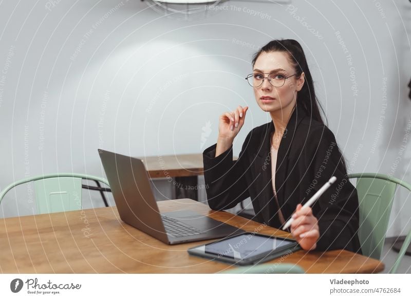 Brunette businesswoman in black suit working on laptop in contemporary office or cafe lifestyle female entrepreneur sitting freelancer internet attractive desk