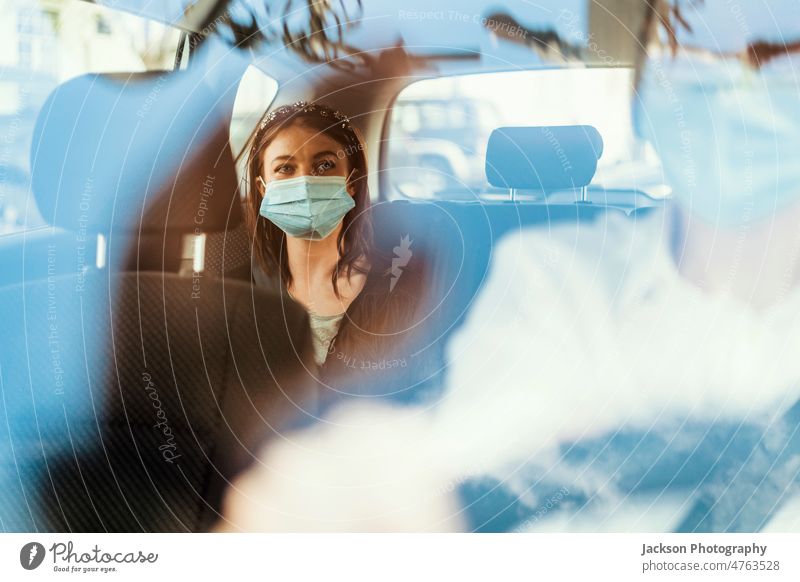 A woman wearing a protective mask on the back seat of a taxi car tourist passenger driver uber client reflection private smile happy discover traveler commuter
