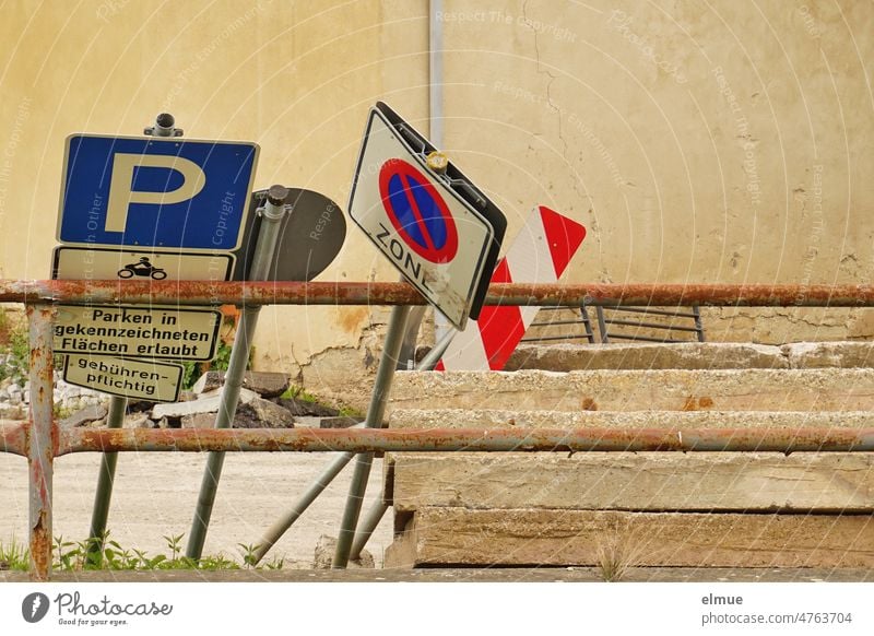several traffic signs and additional signs leaning against a metal barrier next to concrete slabs / storage place for road construction works Road sign