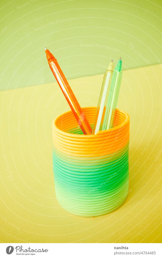 Colorful pens inside a colorful slinky toy fluor childhood remember retro orange green lime yellow flat background abstract chape circle spiral school material