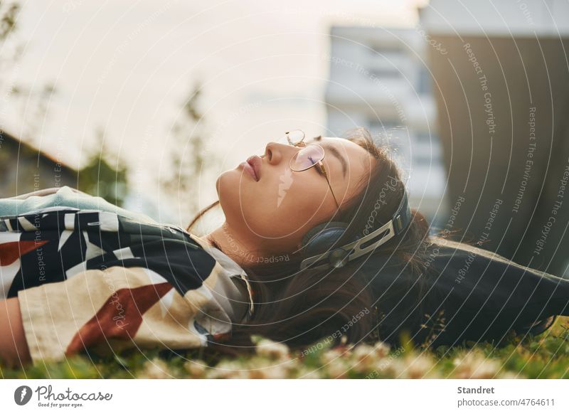 Relaxing on the grass. In headphones. Young asian woman is outdoors at daytime young music lying down adult female japanese chinese korean brown hair beauty