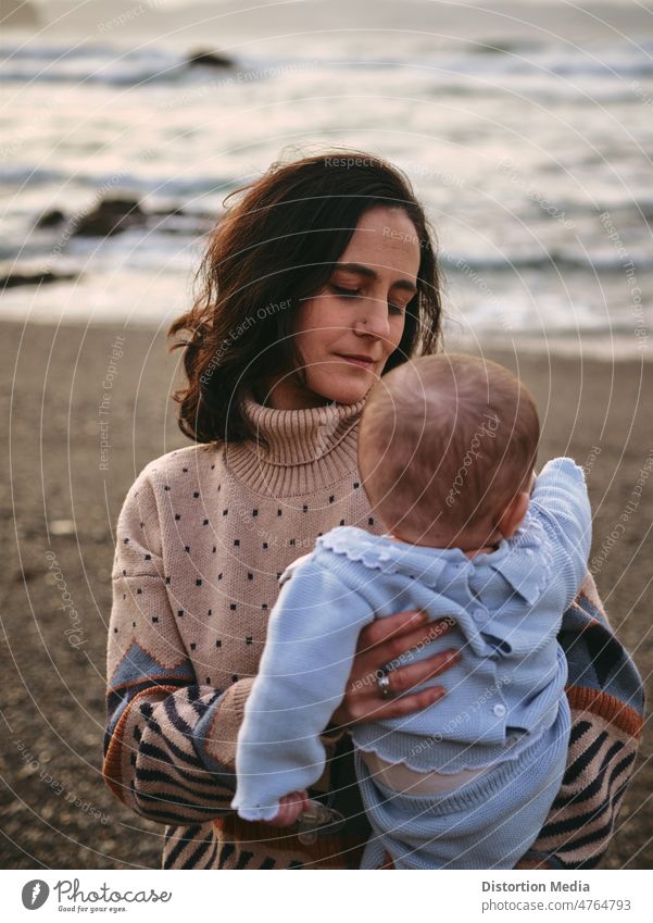 Young mother looking lovingly and tenderly at her baby on the beach, vertically daughters adorable caucasian bonding loving unity communication single mom