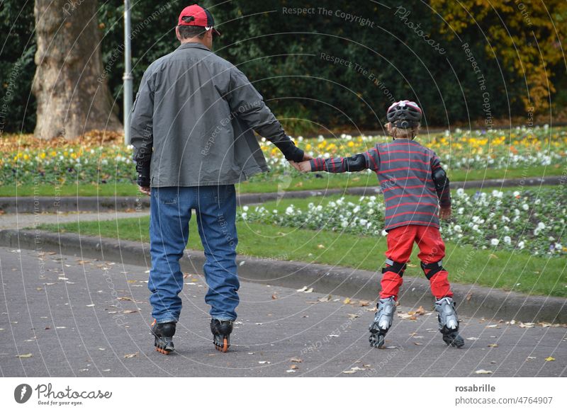 behind | father and son skating hand in hand Leisure and hobbies Inline skates Father's Day Son Sports Joy Inline skating Rollerskating Study Playing Infancy