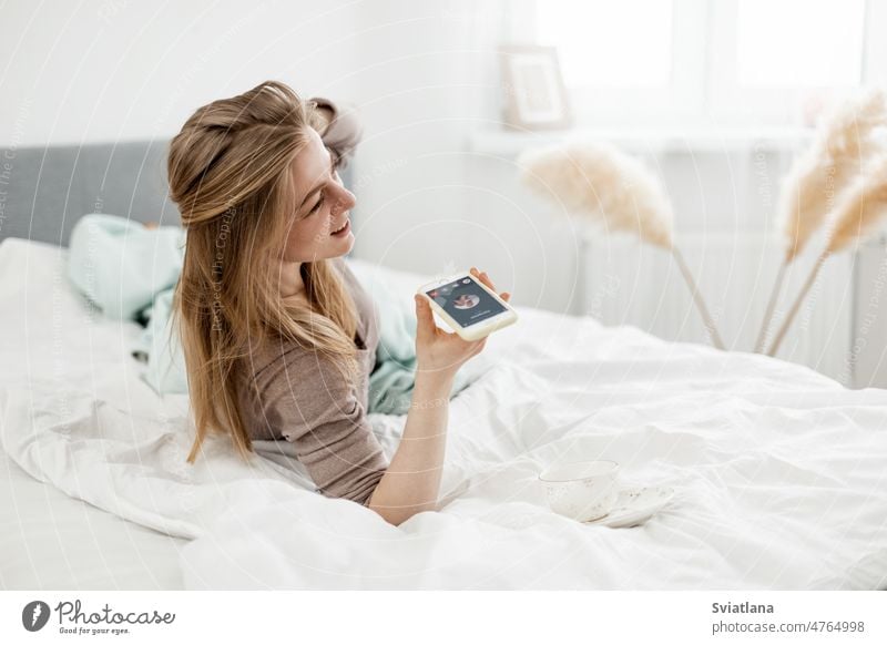 A young woman is talking on the phone on her smartphone in her cozy bed. People and lifestyle conversation morning comfort telephone top mobile cellphone