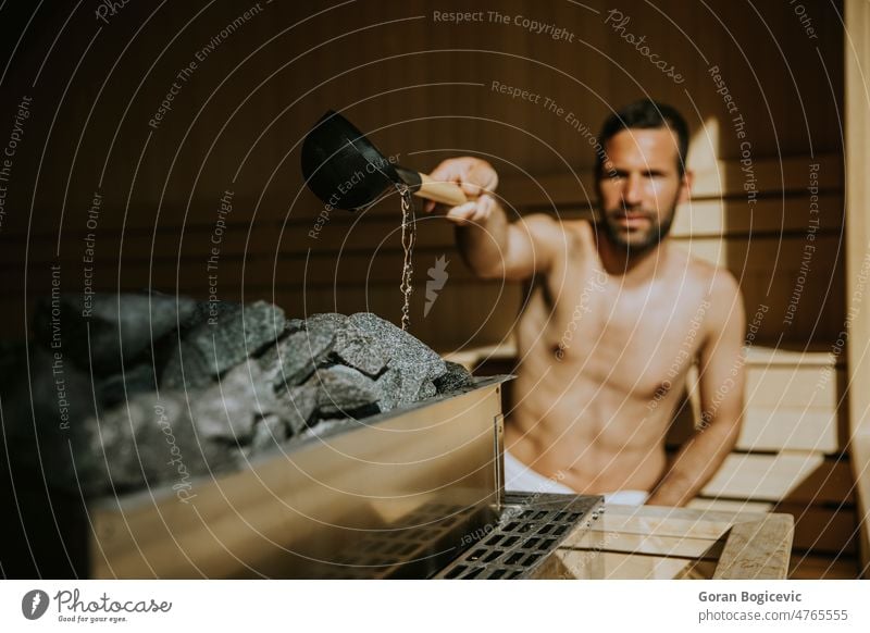 Young man pouring water onto hot stone in the sauna heat young steam spa healthy treatment beauty wood bath bench therapy relaxation wet people wooden activity