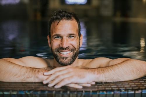 Portrait of smiling young man relaxing by the swimming pool edge handsome man handsome young man poolside male summer swimwear vacation swimmer water sport