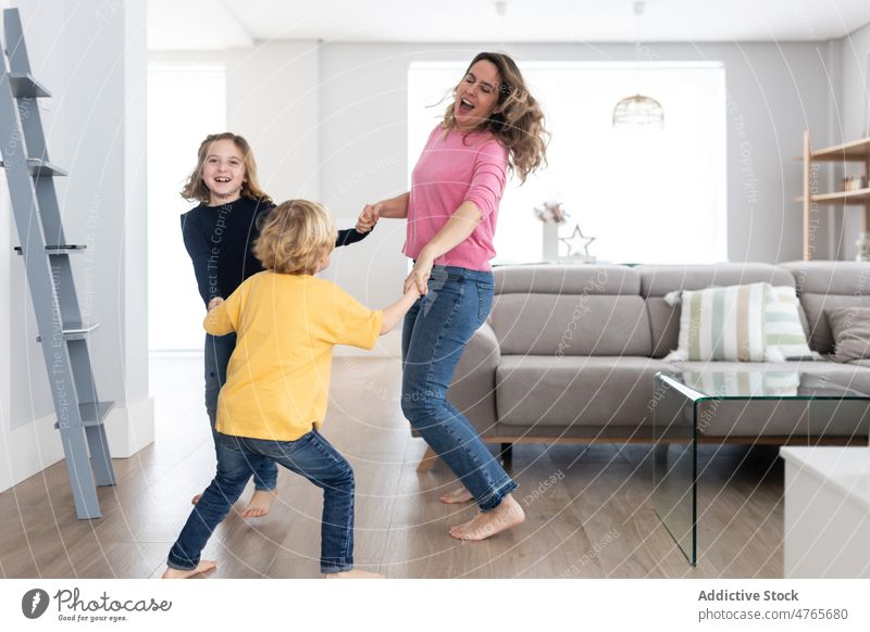 Cheerful mother with children spinning around sibling play pastime spend time living room childhood spin around having fun motherhood bonding together childcare
