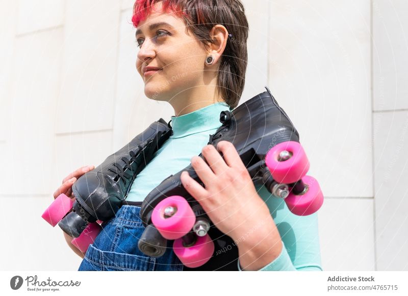 Female carrying rollers against building wall woman roller skate quad roller hobby sporty lifestyle active tile activity female dyed hair casual happy