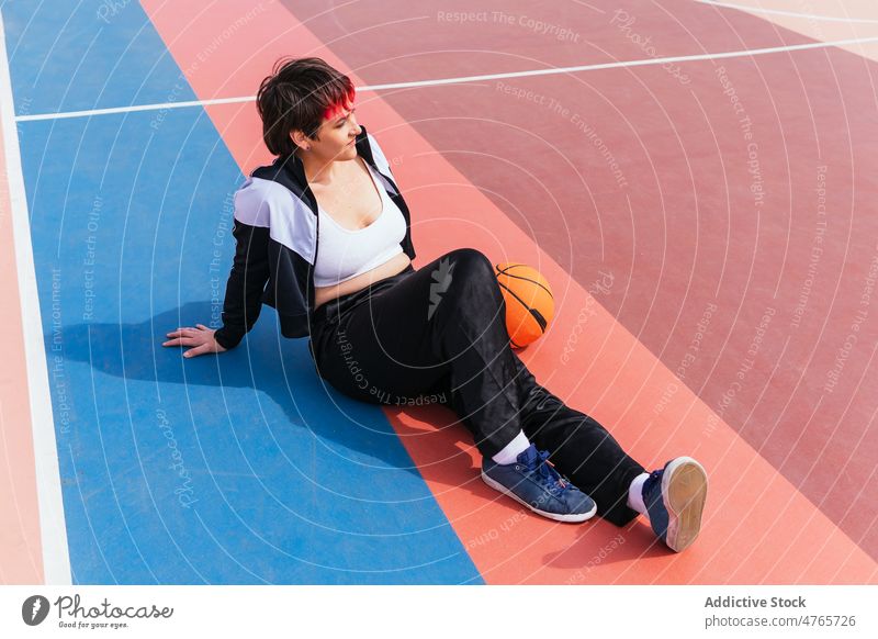 Sportswoman lying on sports ground near basketball sportswoman player streetball break rest game female hobby practice training activity lifestyle fit dyed hair