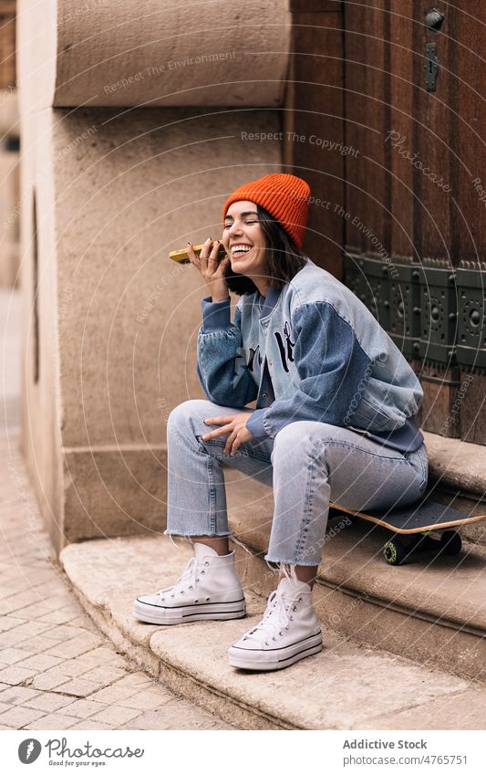 Cheerful woman listening recording voice message on skateboard audio building street street style city hobby urban appearance female town lady garment